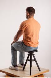 Sitting pose orange thsirt light blue jeans of bodybuilder Harold